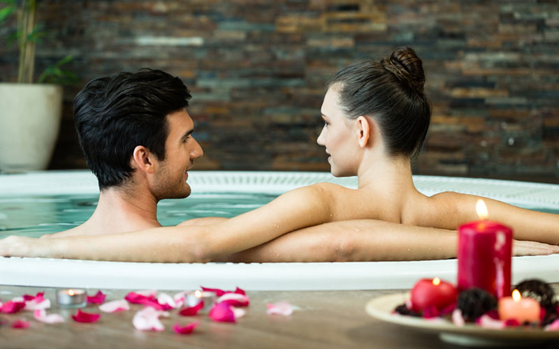 Garçon et fille dans un jacuzzi avec des bougies derrière